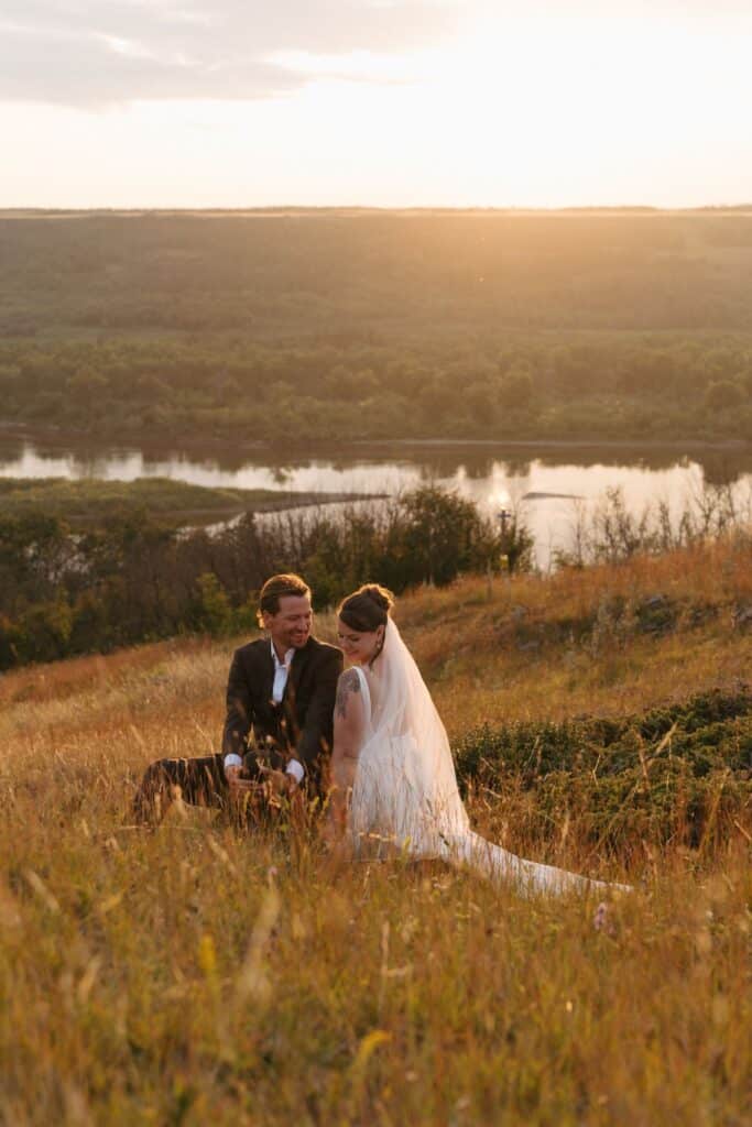 A couple sit together on the ravine edge at golden hour above the river, Blue Sky Ranch wedding